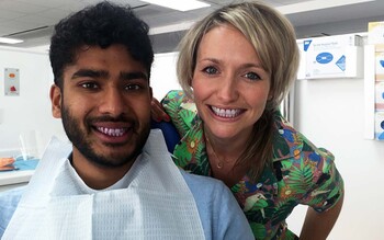 Presenter Kate Quilton stands behind Dr Tamal Ray, who wears a disposable medical apron, in a clinic treatment room.
