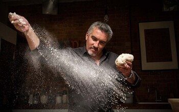Paul Hollywood scatters flour on a kitchen worktop while holding a ball of dough.
