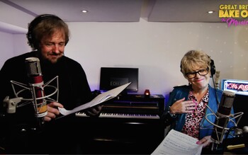 John Owen-Jones and Rosemary Ashe stand with lyric sheets at microphones in a recording studio.