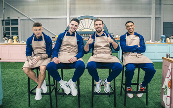 Jordan Henderson, Declan Rice, Kieran Trippier and Trent Alexander-Arnold sitting on stools in a specially constructed version of the Bake Off tent, inside the training ground 